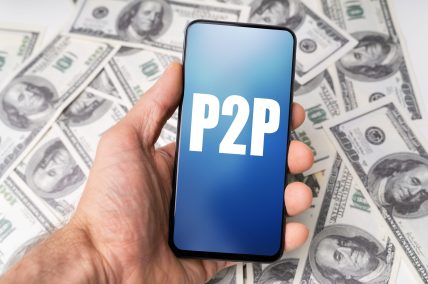 Person's Hand Holding Mobile Phone With P2p Text Against Dollar Bills Background